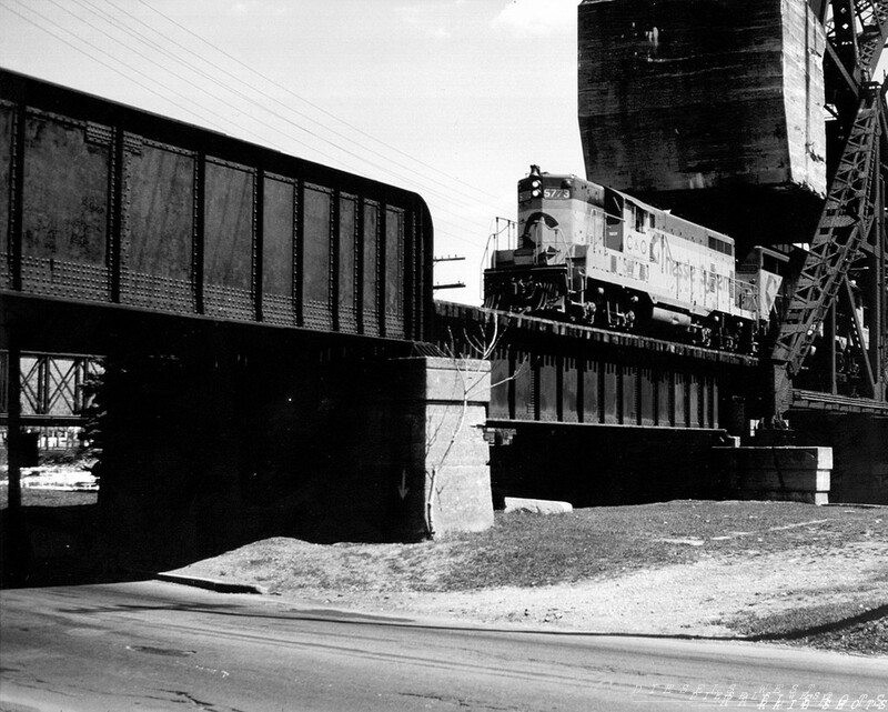 Class of '51
C&O GP7 #5773, a graduate of the EMD class of 1951, leads Chessie System's CG-41 beneath the massive concrete counterweight of the ex-NYC lift bridge across the Erie Canal separating the small Western NY cities of Tonawanda and North Tonawanda, midway between Buffalo and Niagara Falls.  The bridge on the parallel ex-EL Niagara Falls branch can be seen at left.  On the far (Tonawanda) side of the bridge was Conrail CP EL-3, where Lehigh Valley trains, prior to April 1. 1976, would access trackage rights on Penn Central's ex-NYC Niagara Branch to reach Niagara Falls and Canadian connections.
Photo Copyright 2008 Tim Baldwin
Keywords: gp7;c&o;5773;chessie;cg-41;bridge;erie;canal;tonawanda;buffalo